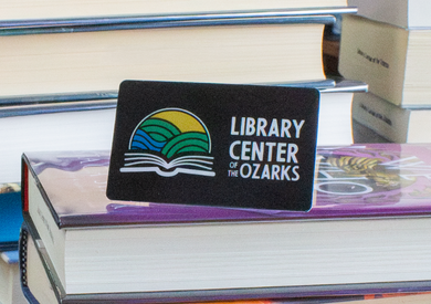 A Library Center of the Ozarks library card propped on books.